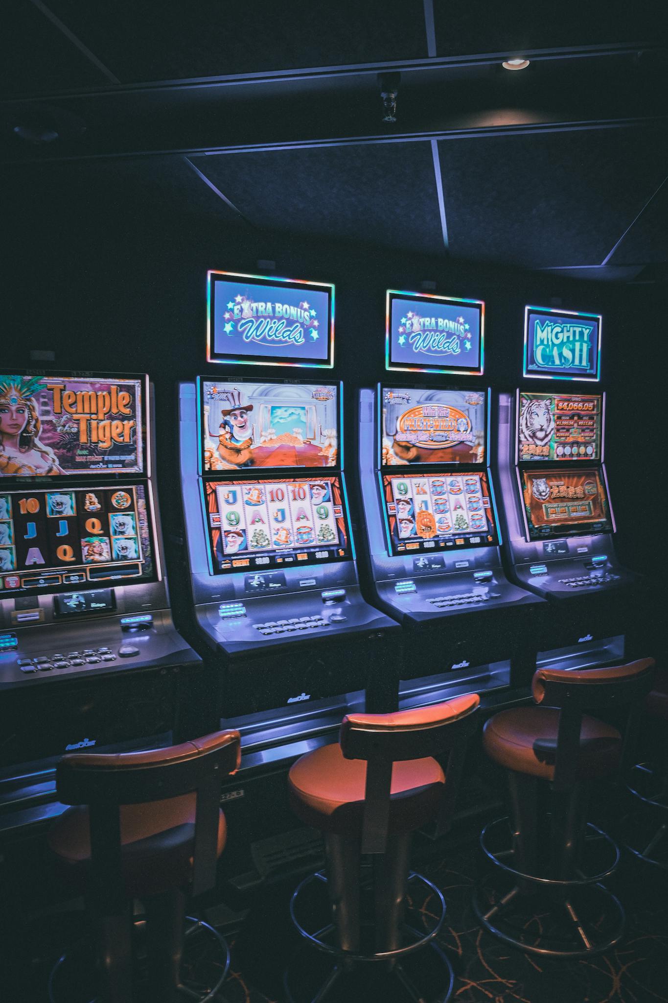 Row of illuminated slot machines in a dimly lit, empty casino area.